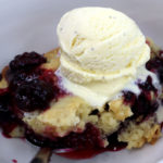berry cobbler served in a white bowl with vanilla ice cream on top.
