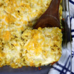 serving cheesy chicken and rice from a glass dish with a wooden spoon.