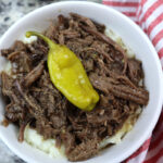 mississippi pot roast on top of mashed potatoes, in a white bowl.