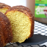 apple cider donut cake slice on a black spatula, with apple cider gallon in the background.