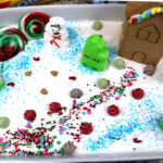 snow dirt cake in white pan decorated with mini gingerbread house.