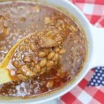 baked beans served from a white baking dish on a wooden spoon.