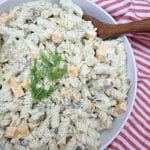 pickle pasta salad served with a wooden spoon in a large white bowl.