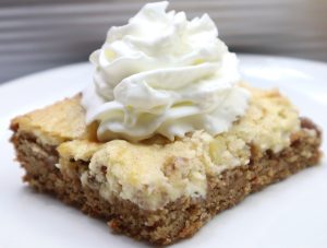 carrot cake gooey bars slice on a white cake with whipped cream on top.