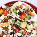 cucumber greek salad in a red bowl with a large white spoon.