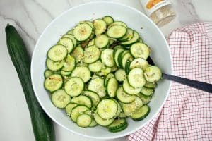Asian cucumber salad in a large white bowl with black spoon.