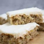 zucchnii bars with cream cheese frosting slices stacked on brown parchment paper.