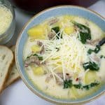 Zuppa Toscana served in a blue bowl with a black spoon, parmesan, and bread.