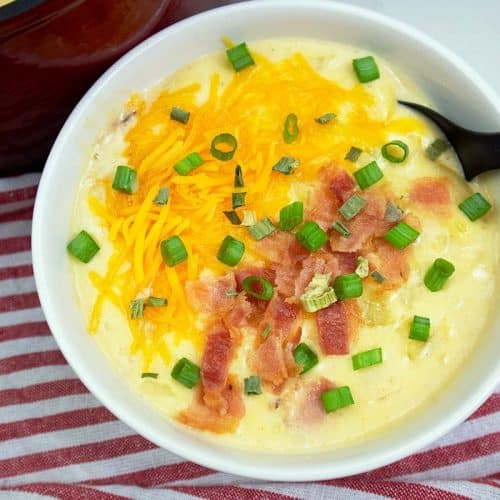 Loaded potato soup served in a white bowl with black spoon.
