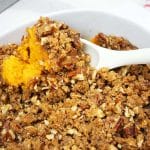 Sweet potato casserole served in a white baking dish with a white spoon.