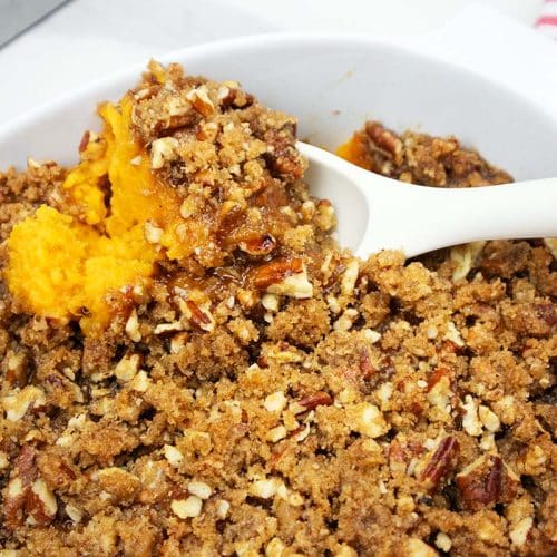 Sweet potato casserole served in a white baking dish with a white spoon.