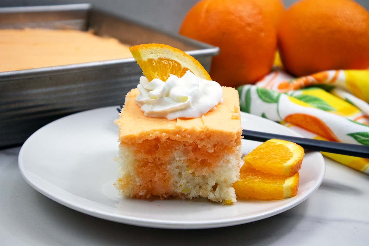 Slice of orange creamsicle cake with whipped cream and orange slice on top.