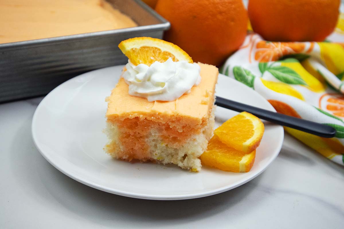 Slice of orange creamsicle cake with whipped cream and orange slice on top.