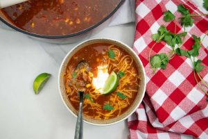 Chicken Tortilla Soup served in a white bowl, cheese and lime on top.