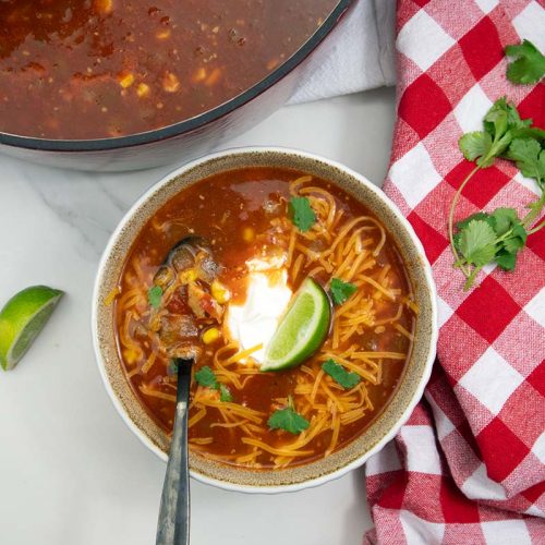 Chicken Tortilla Soup served in a white bowl, cheese and lime on top.