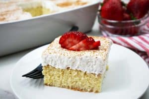Tres Leche Cake slice with cinnamon and strawberries on top.