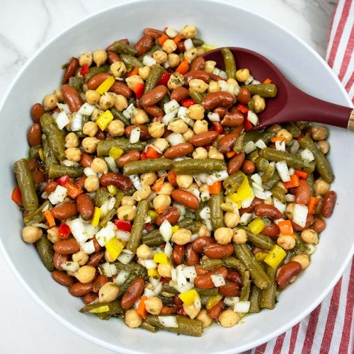 Three Bean Salad in a white bowl with red and wood serving spoon.