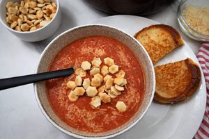 homemade tomato soup served with grilled cheese and crackers in a tan bowl.