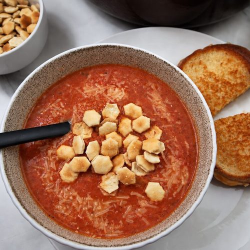 homemade tomato soup served with grilled cheese and crackers in a tan bowl.